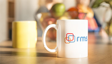 Auf einem Tisch steht ein Kaffeebecher mit dem Logo der rms